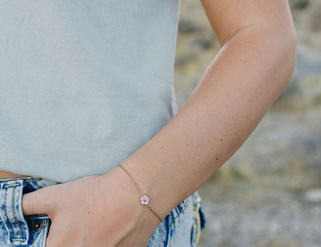 Desert Sol Petal Bracelet in gold with a pink crystal flower on a wrist by a jeans pocket