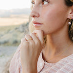 Model wearing the Desert Sol Petal Hoop Earrings with a pink crystal flower, desert hills behind her