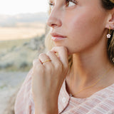 Model wearing the Desert Sol Petal Hoop Earrings with a pink crystal flower, desert hills behind her