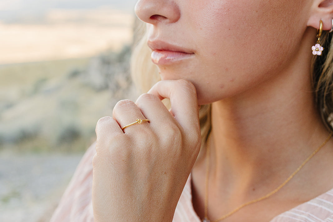 Model wearing the Desert Sol Petal Hoop Earrings with a pink crystal flower, desert hills behind her