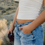 Desert Sol Meadow Ring worn on a hand in a jeans pocket, with a plum crystal silk scrunchie in the other hand