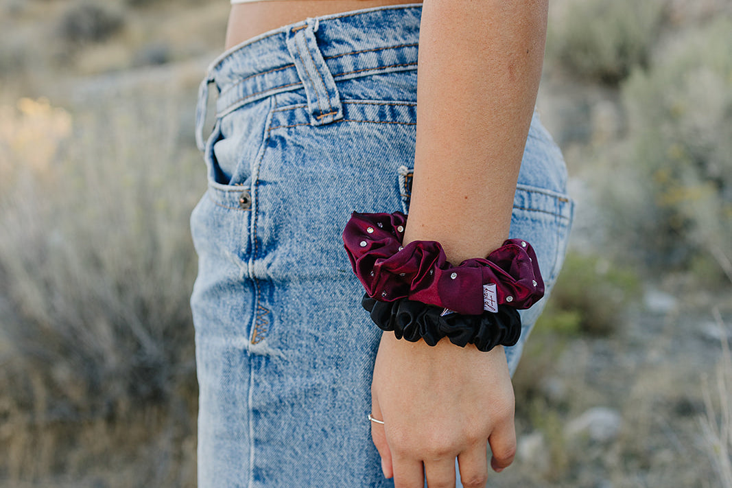 Desert Sol Crystal Silk Scrunchies in Plum and Black worn stacked on a wrist