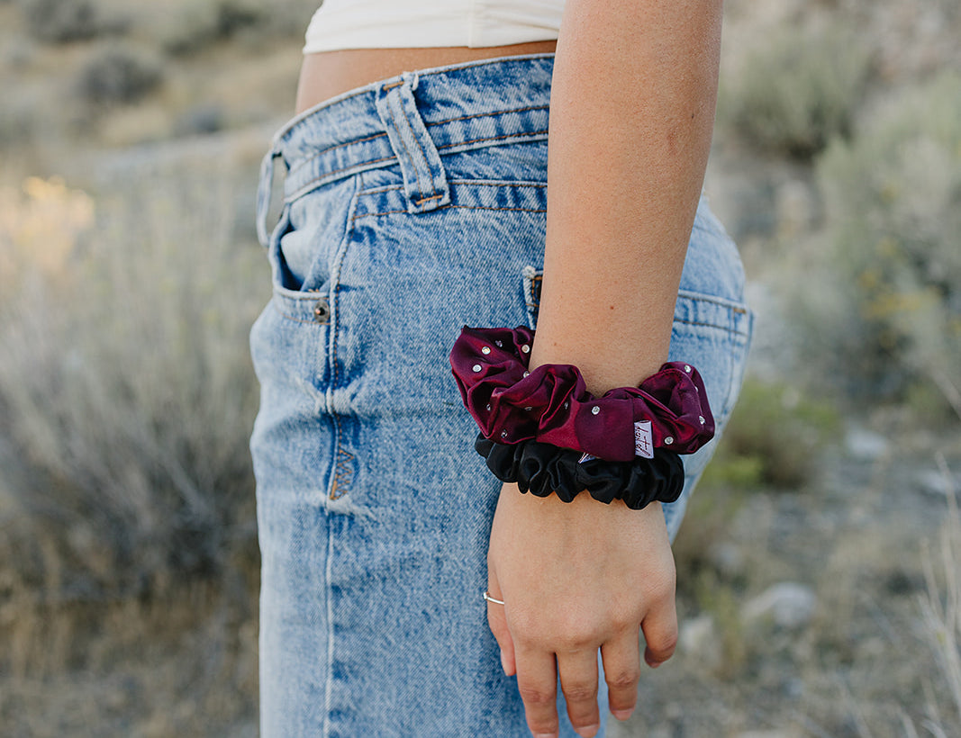 Desert Sol Crystal Silk Scrunchies in Plum and Black worn stacked on a wrist