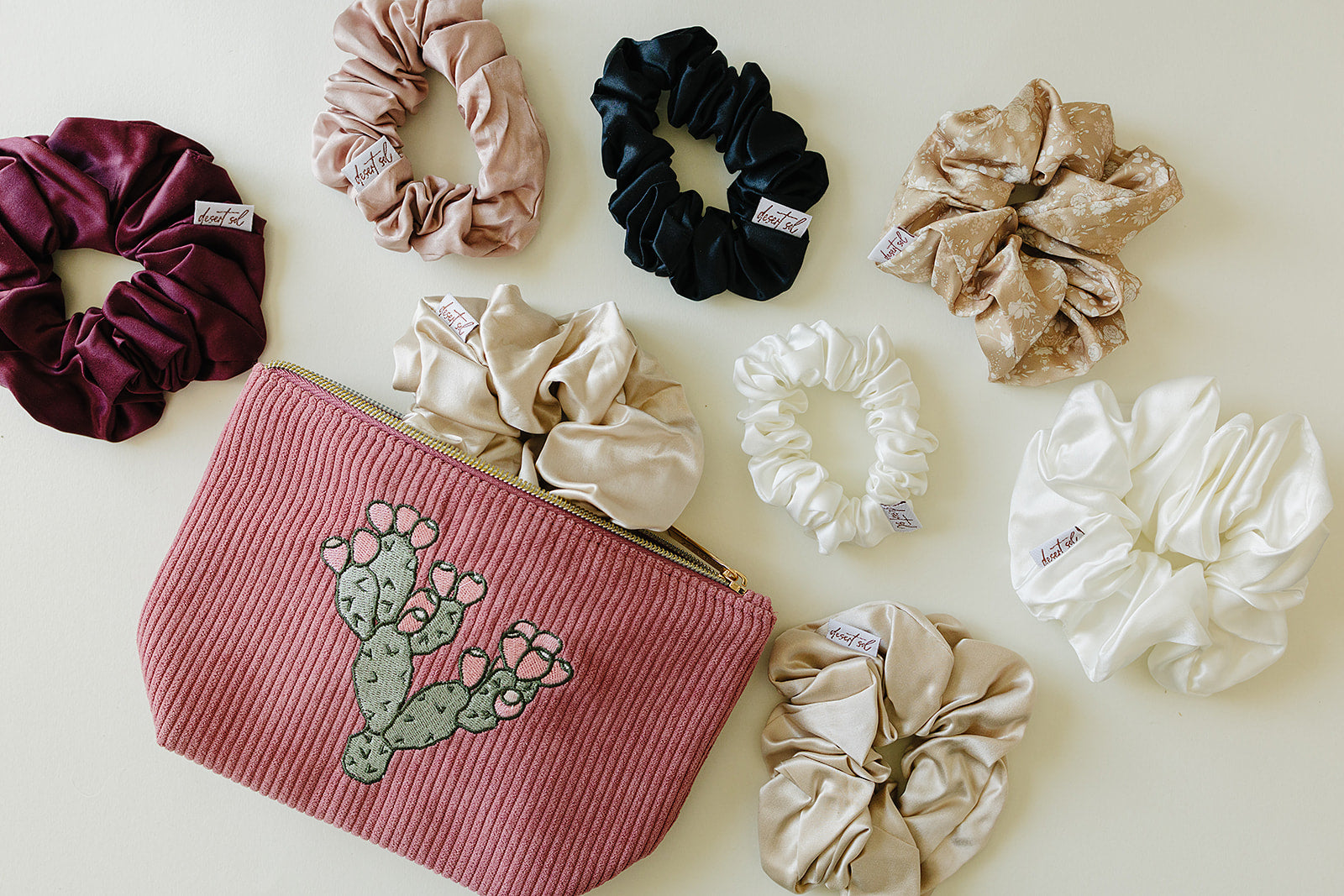 Desert Sol Prickly Mauve Pear corduroy pouch surrounded by silk scrunchies in plum, black, champagne and ivory