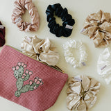 Desert Sol Prickly Mauve Pear corduroy pouch surrounded by silk scrunchies in plum, black, champagne and ivory