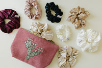 Desert Sol Prickly Mauve Pear corduroy pouch surrounded by silk scrunchies in plum, black, champagne and ivory