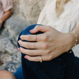 Desert Sol Meadow Ring and a gold Solara pearl bracelet on a hand resting on a knee