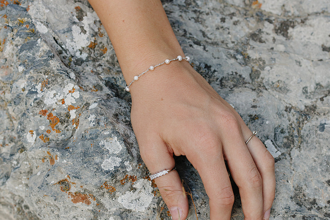 Desert Sol Solara pearl bracelet in silver and Canyon Marquise Ring on a hand resting on gray rock