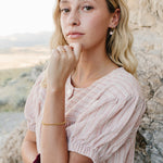 Model wearing the Desert Sol Meadow Ring with a gold chain bracelet, chin resting on her hand against desert rock