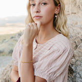 Model wearing the Desert Sol Meadow Ring with a gold chain bracelet, chin resting on her hand against desert rock