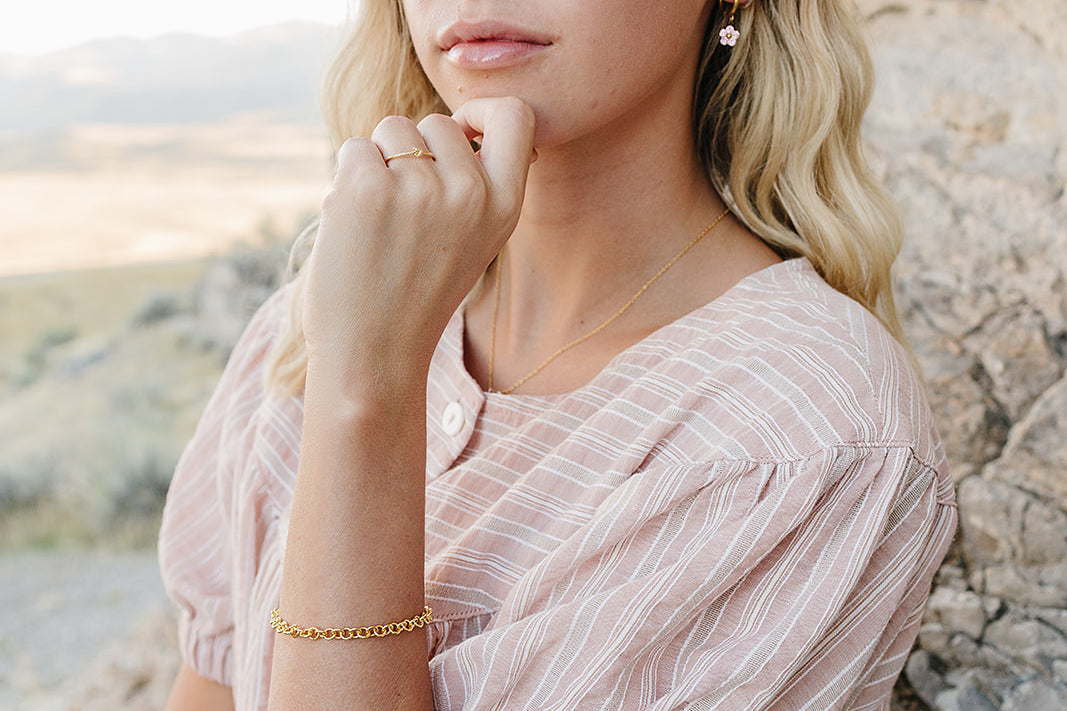 Model wearing the Desert Sol Meadow Ring with a gold chain bracelet, chin resting on her hand against desert rock