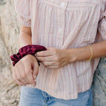 Desert Sol Meadow Ring with a gold chain bracelet and a plum silk scrunchie on the wrist, worn with a pink striped top