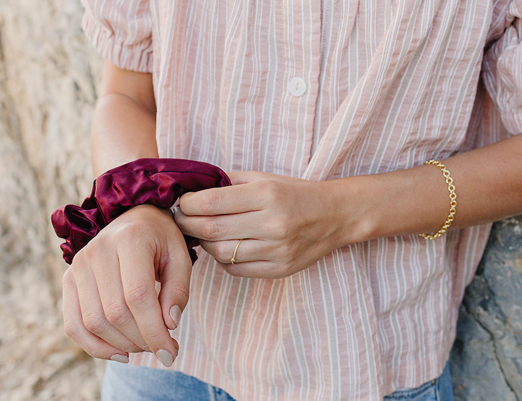 Model wearing the Desert Sol Sundown Chain Bracelet in gold with a plum Mulberry Silk Scrunchie on her wrist