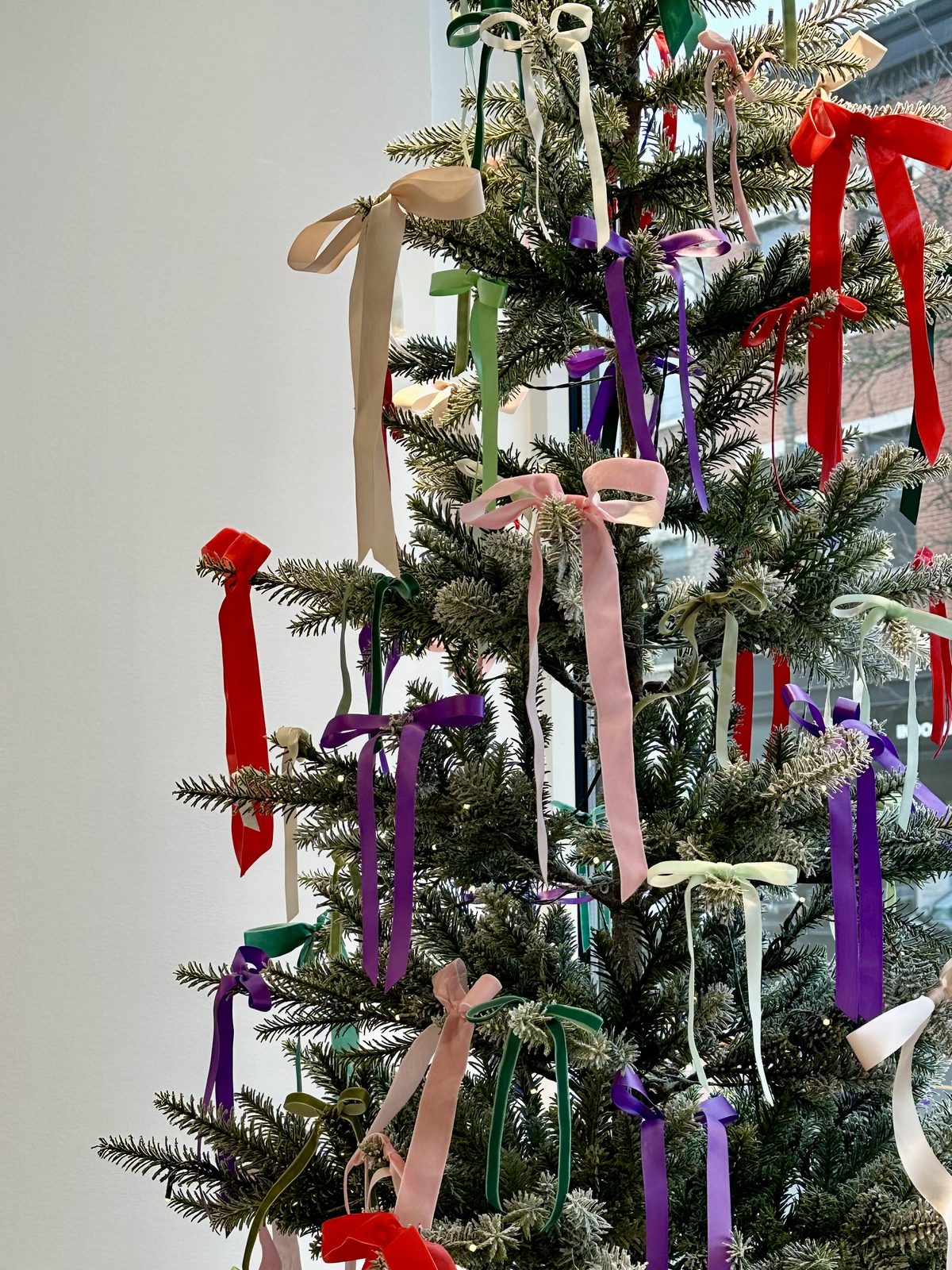 Flocked Christmas tree trimmed with velvet ribbon bows in pink, red, purple, green and cream