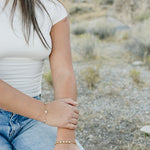 Desert Sol Wildflower Daisy Chain Bracelet and Wild Bloom Bracelet in gold on a model kneeling in the desert