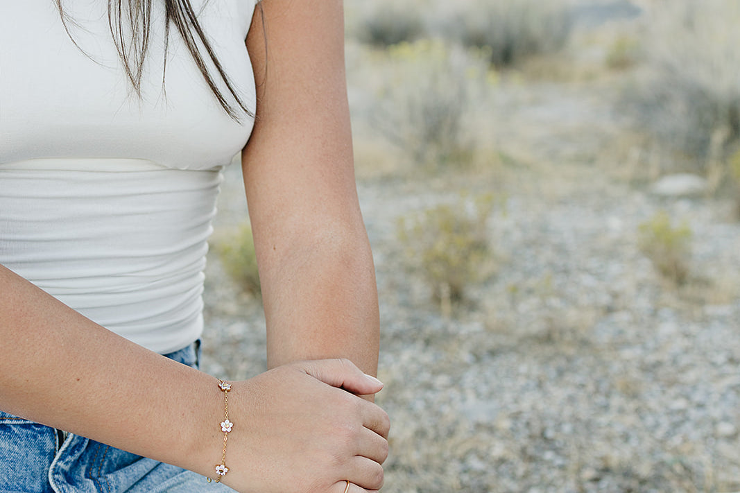 Desert Sol Wildflower Daisy Chain Bracelet and Wild Bloom Bracelet in gold on a model kneeling in the desert