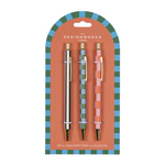 A Dopo Pen Set of 3, three patterned ballpoint pens, one gold, one green striped and one pink patterned, on a blue and green checkered backer card