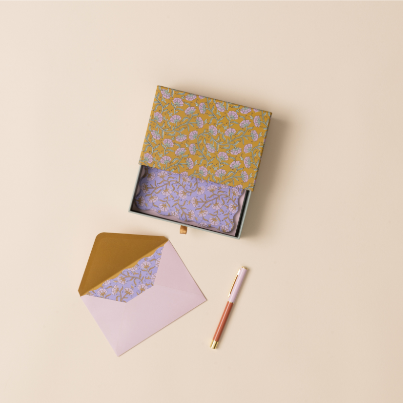 Designworks Notecards Set of 16, open mustard floral box with a purple floral card, pink envelope and pen
