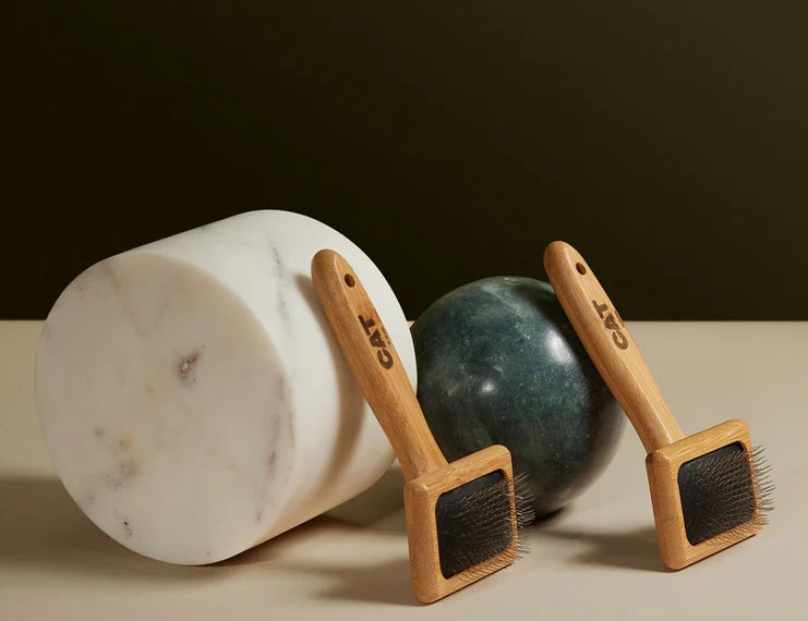 Two DOG by Dr Lisa Cat Slicker Brushes leaning on marble and green stone blocks