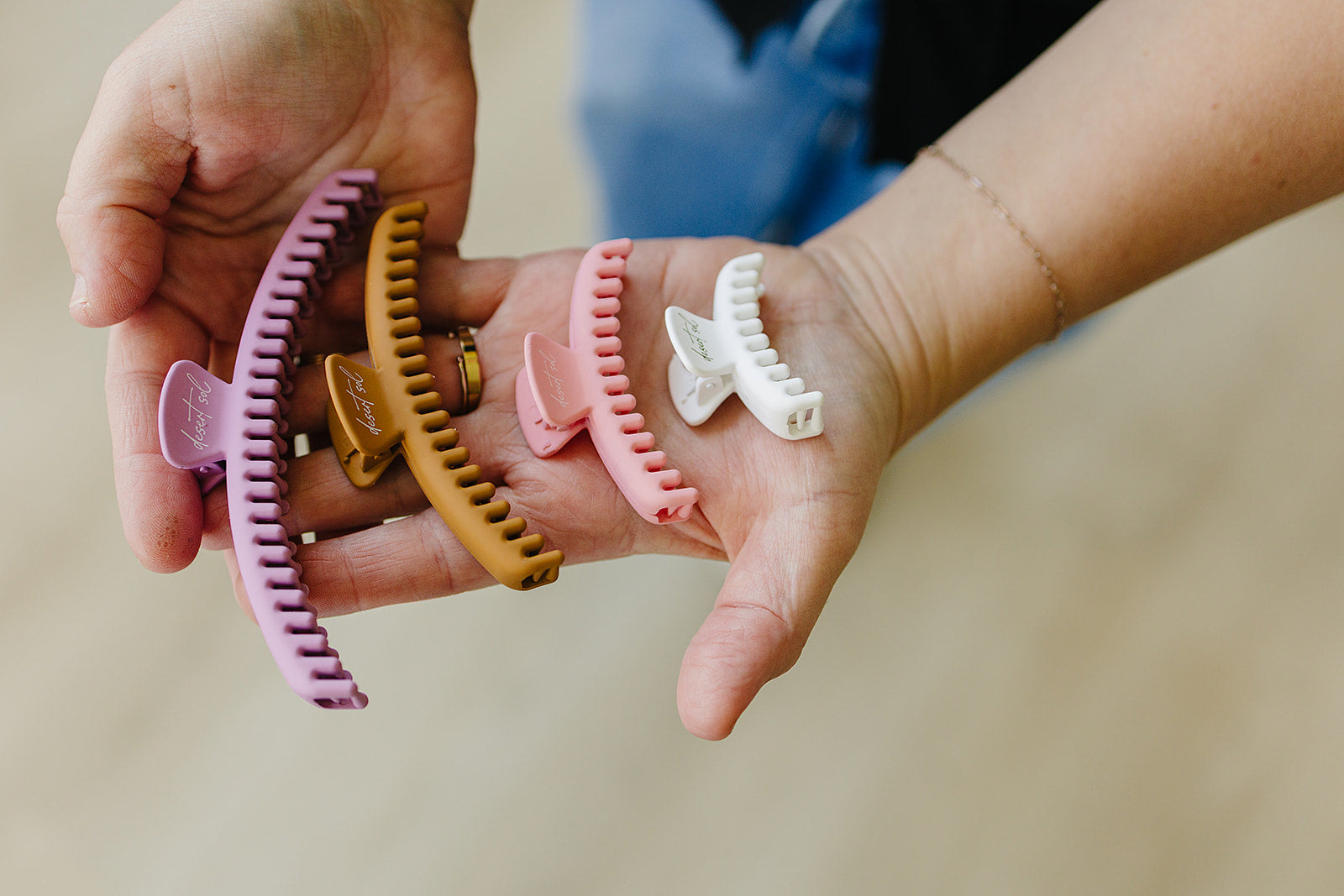 Four Frenchie matte claw clips in mauve, Honey, Blossom, and White, held in cupped hands.