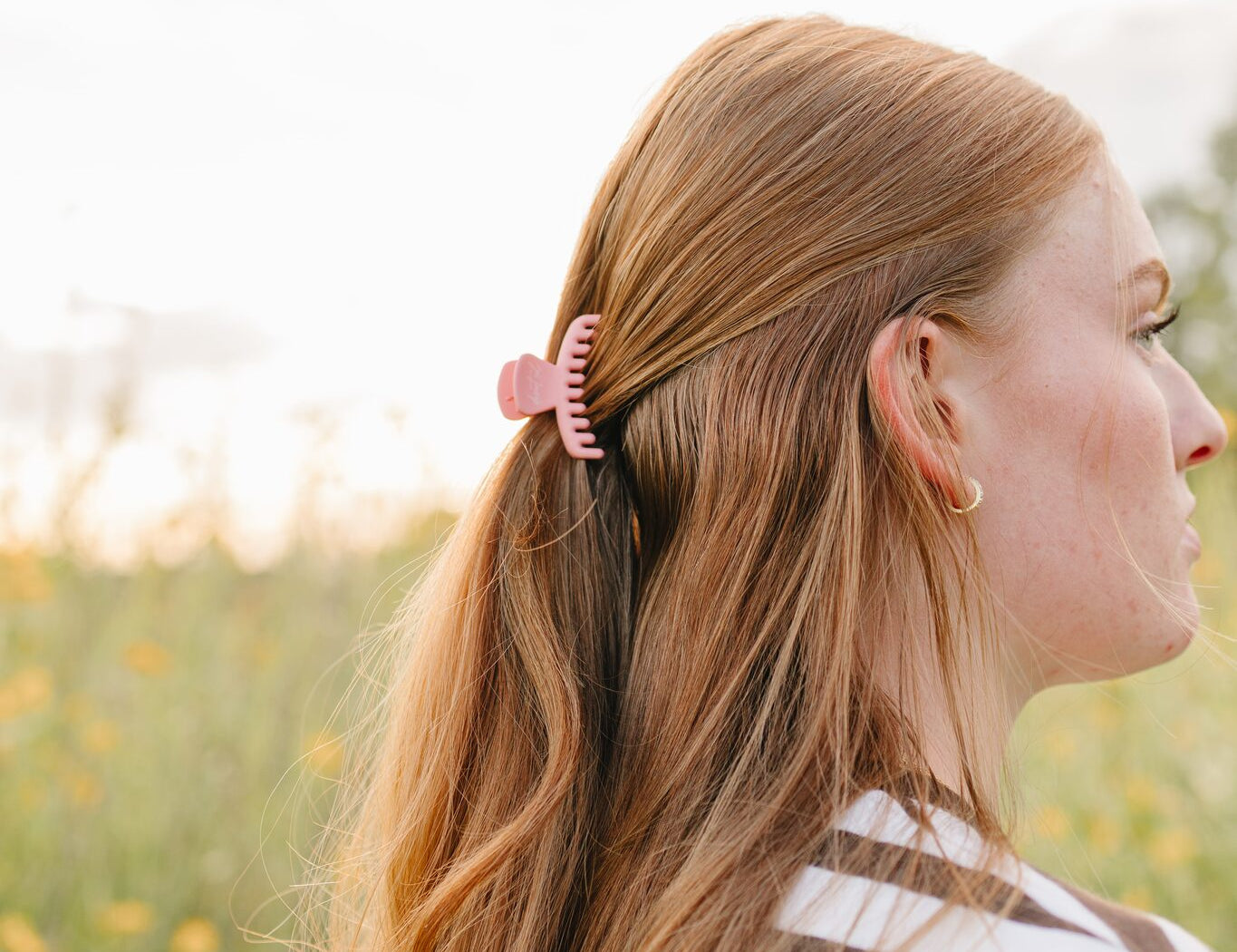 The Petal Frenchie claw clip in petite size holding a half up section of long blonde hair, worn outdoors.