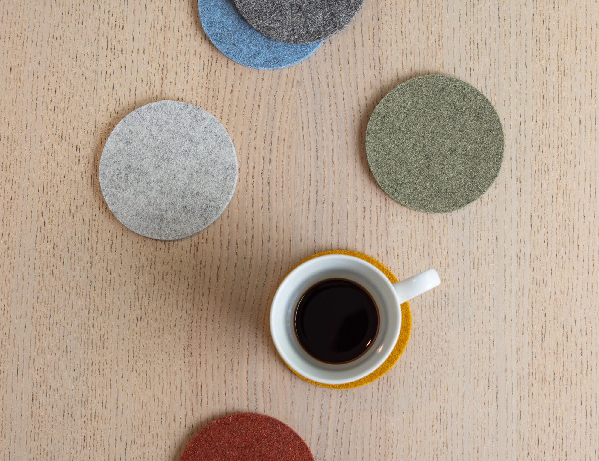 Graf Lantz Bierfilzl Merino Wool Round Coasters in gray, green, blue and red on a wood table with a coffee cup