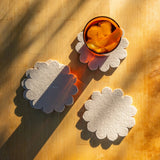 Graf Lantz Coaster Crest scalloped felt coasters in cream under an amber glass on a sunlit wooden table