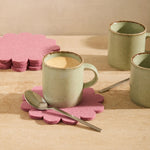 Graf Lantz Coaster Crest in Mauve under a sage mug on a wooden table with a spoon