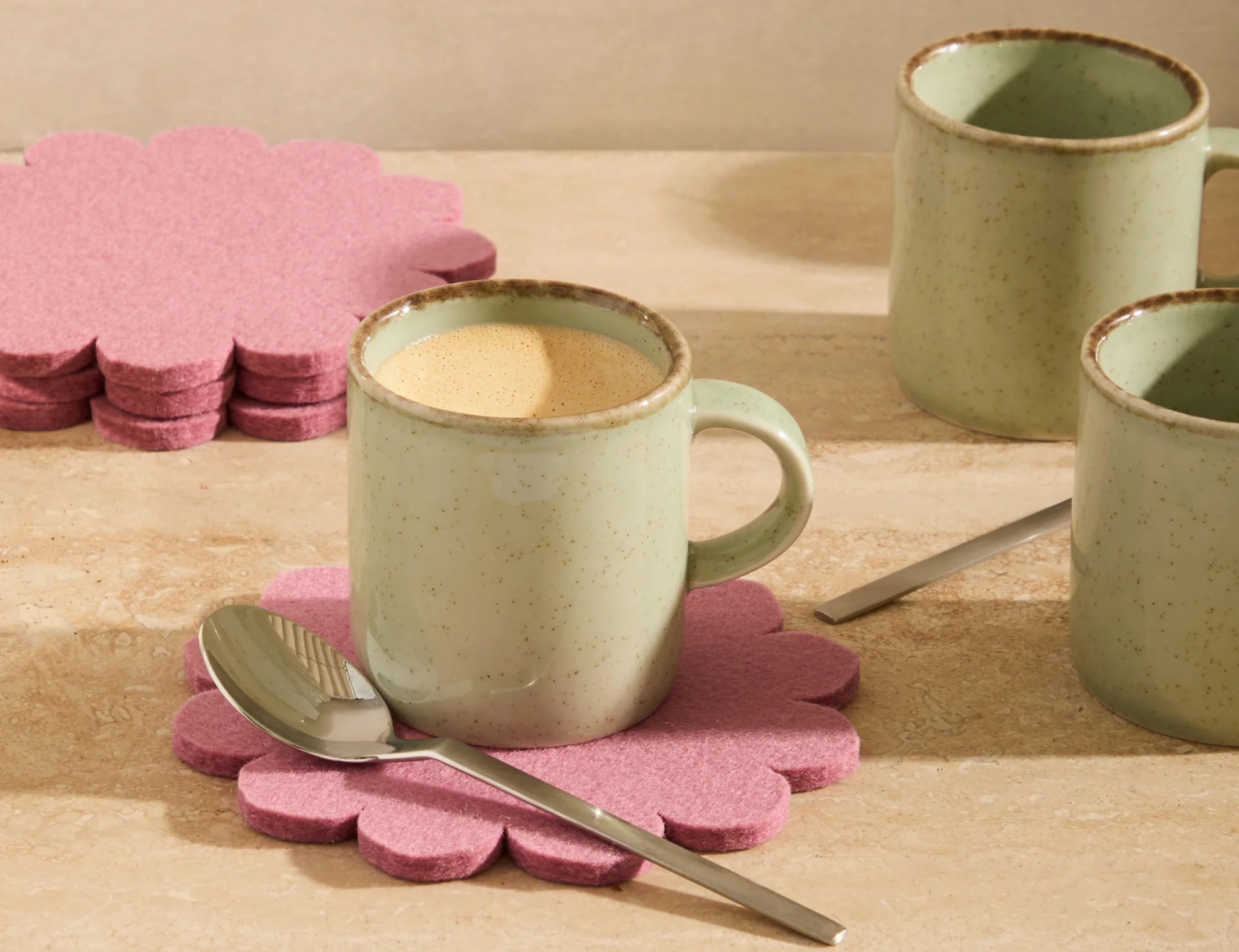 Graf Lantz Coaster Crest in Mauve under a sage mug on a wooden table with a spoon