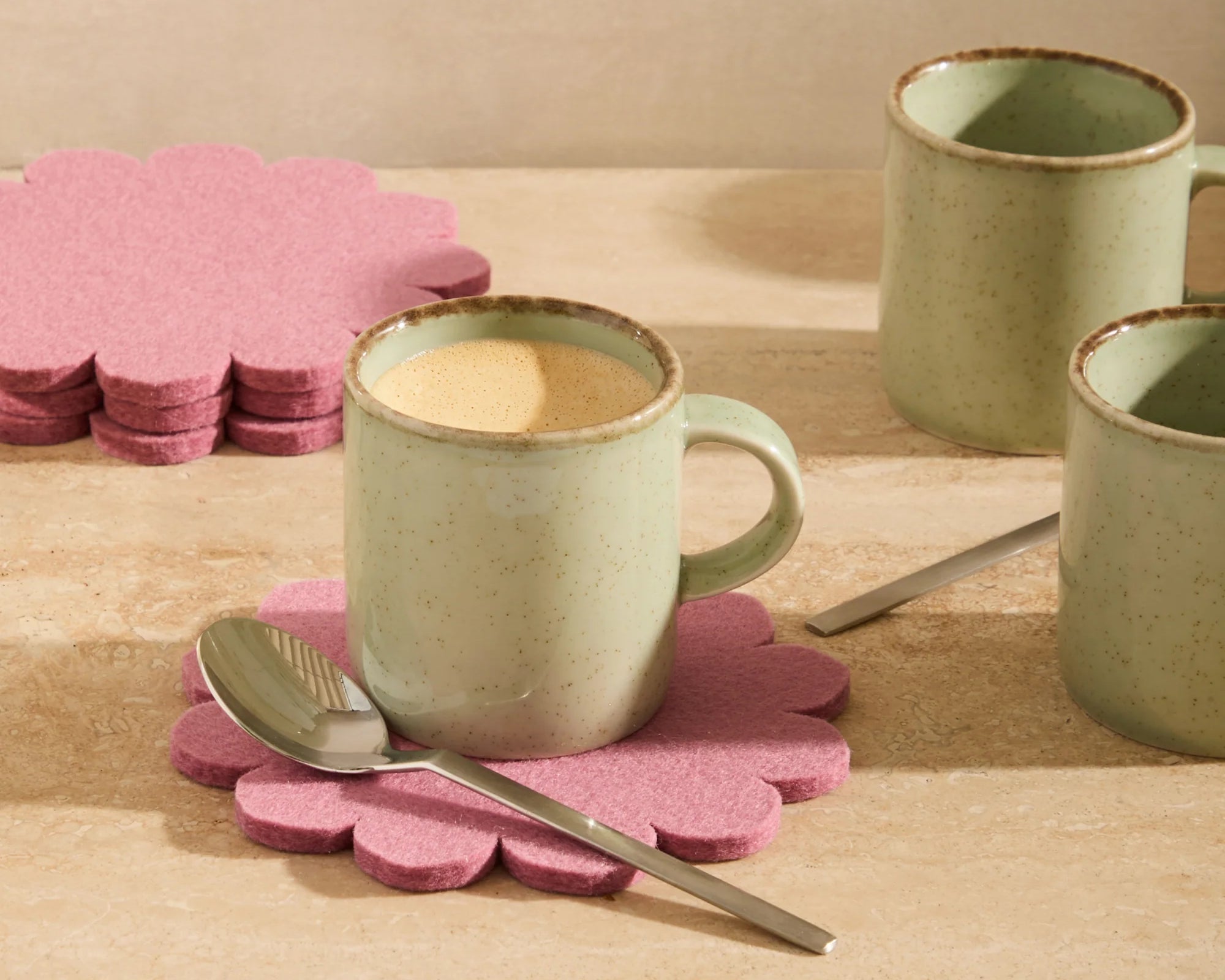 Graf Lantz Coaster Crest in Mauve under a sage mug on a wooden table with a spoon