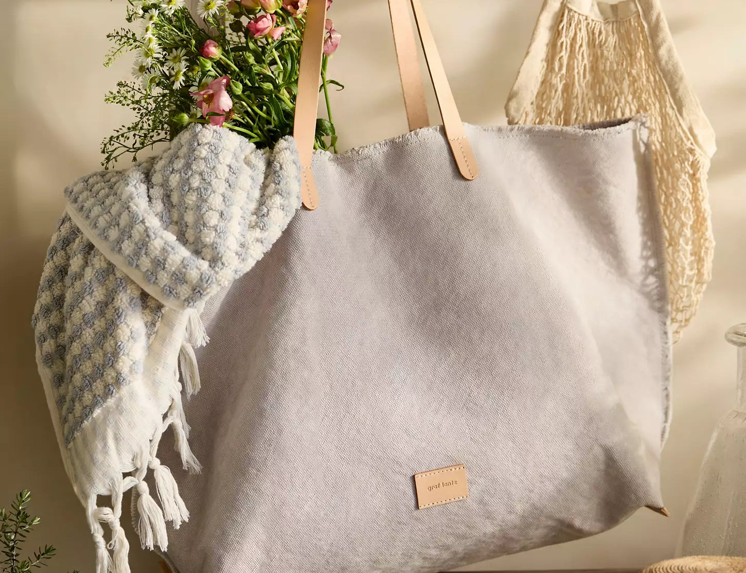 Graf Lantz Hana Canvas Boat Bag in gray with leather handles, hanging with a blanket and flowers inside