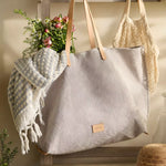 Graf Lantz Hana Canvas Boat Bag in gray with leather handles, hanging with a blanket and flowers inside