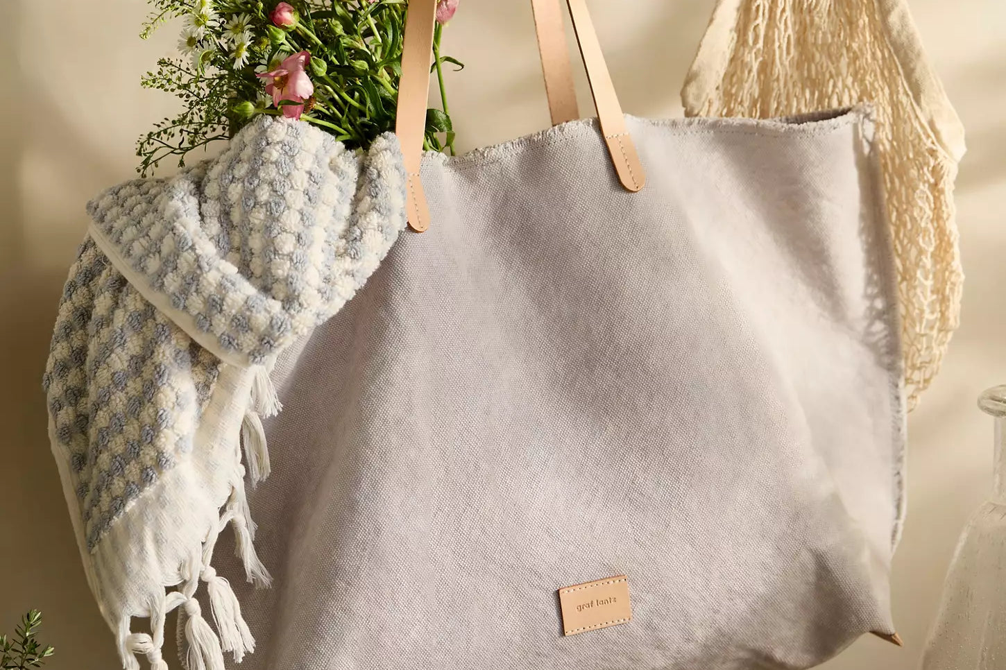 Graf Lantz Hana Canvas Boat Bag in gray with leather handles, hanging with a blanket and flowers inside