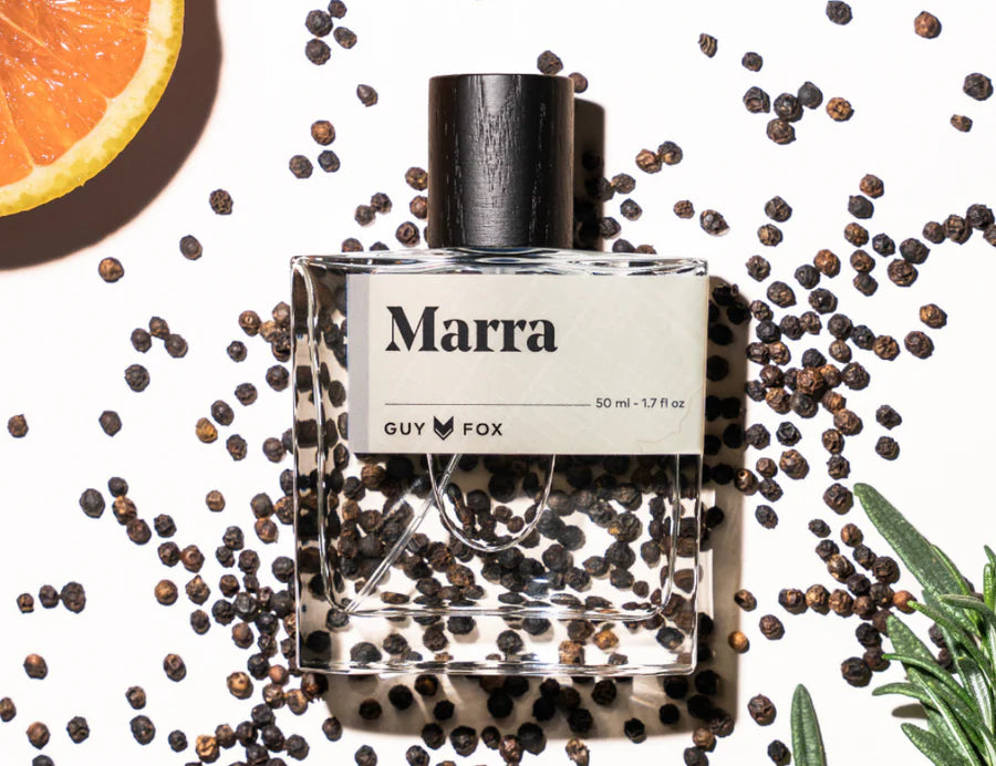 Guy Fox Marra Cologne bottle surrounded by black peppercorns, orange and rosemary