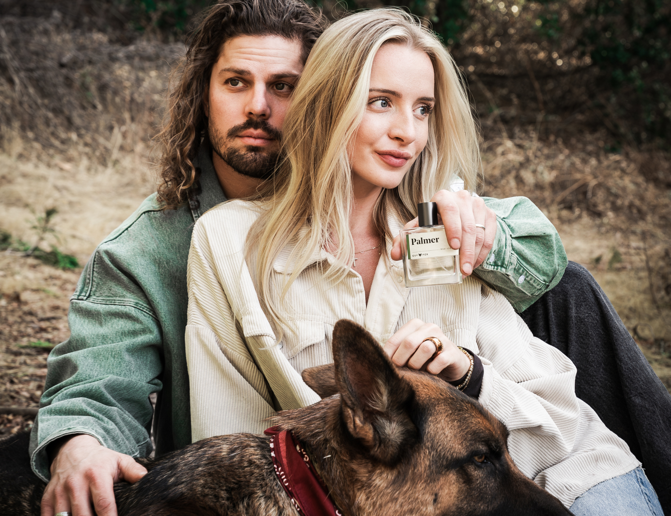 Couple sitting outdoors with a German shepherd, the woman holding Guy Fox Palmer Men's Cologne