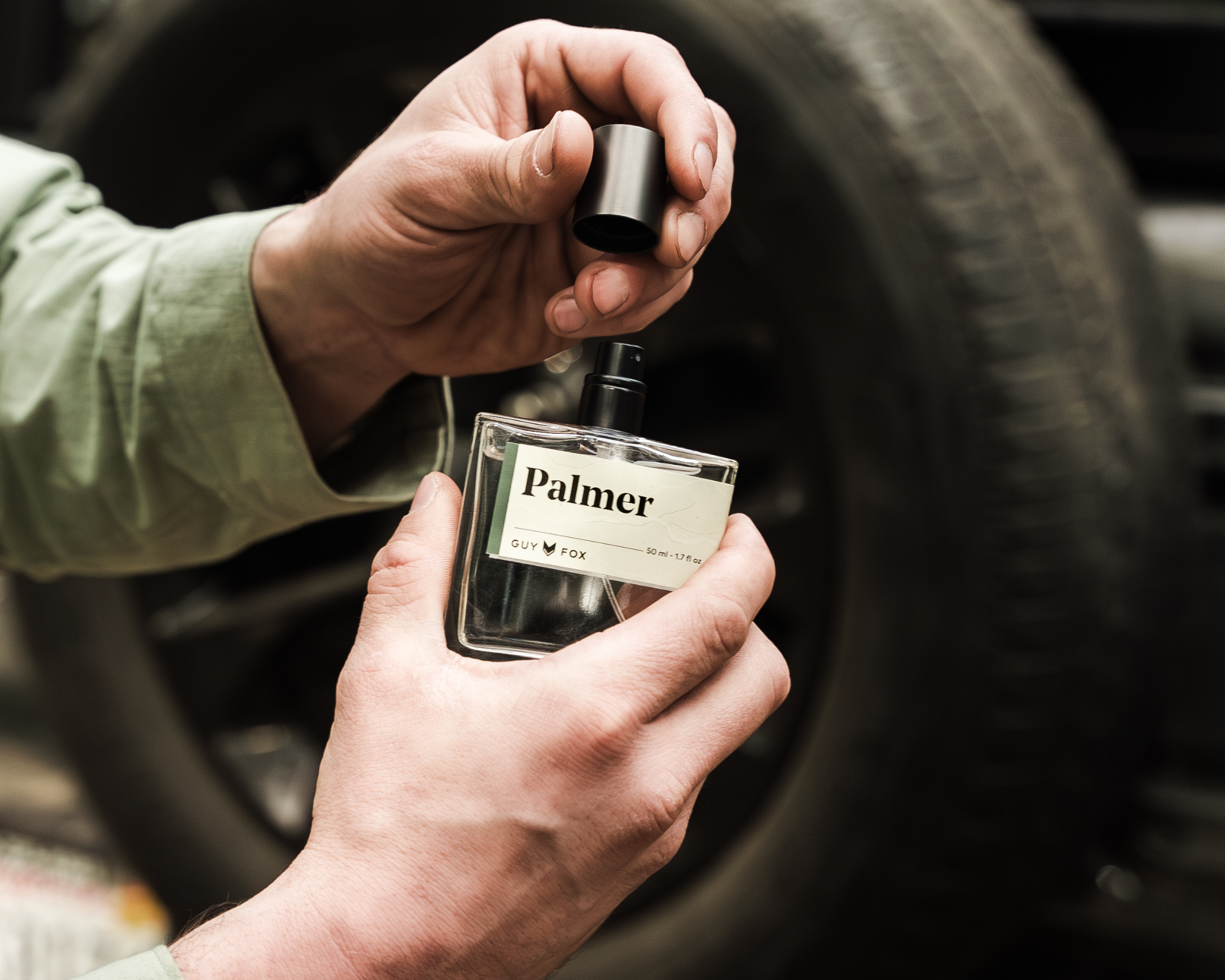 Hands uncapping the Guy Fox Palmer Men's Cologne bottle beside a truck tire