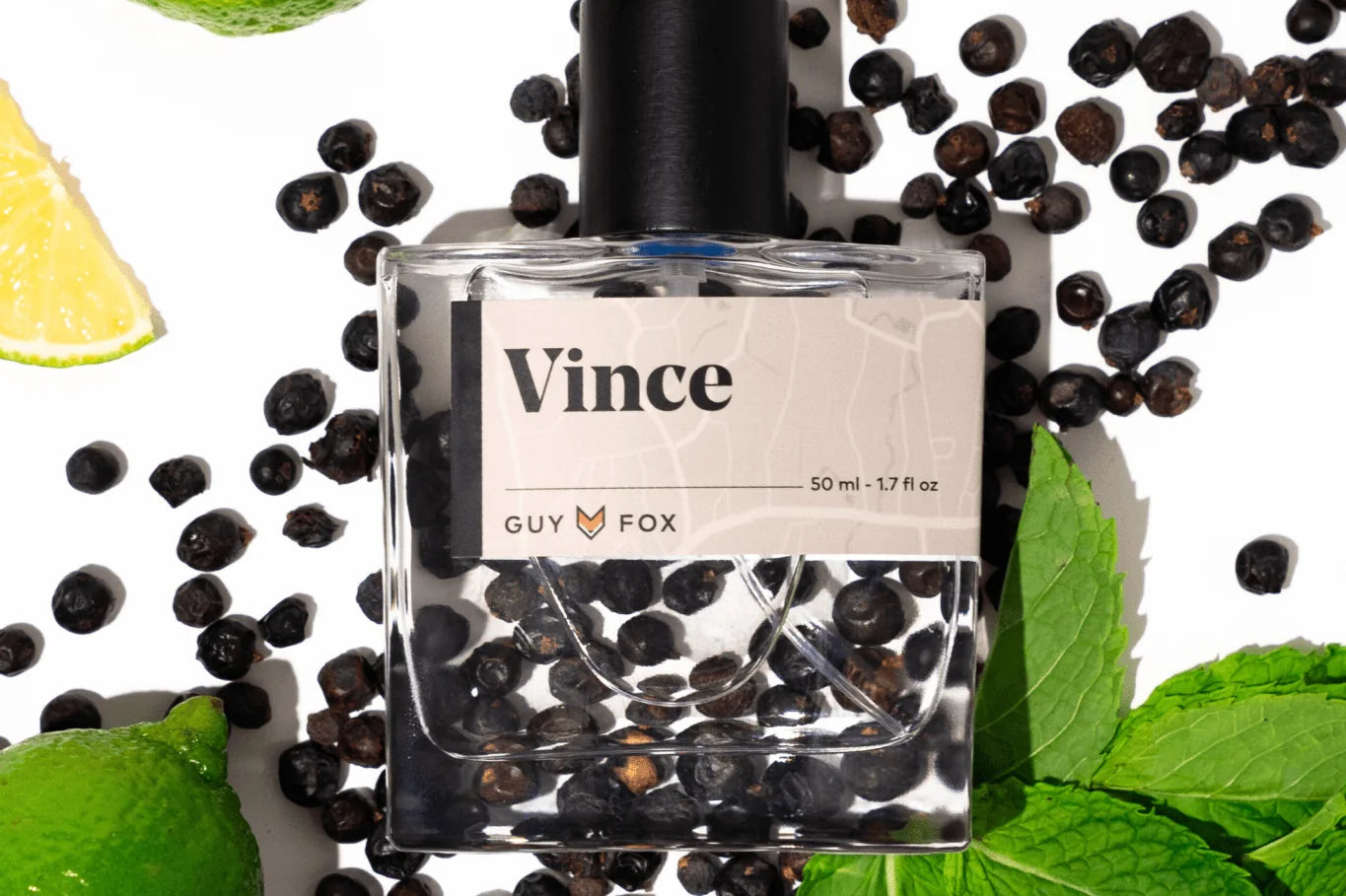 Guy Fox Vince Cologne bottle lying among black peppercorns, mint leaves and lime slices