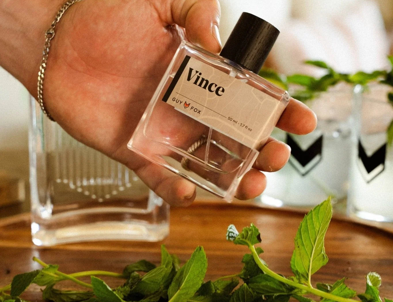 Hand holding the Guy Fox Vince Cologne bottle over a tray of mint and drinks