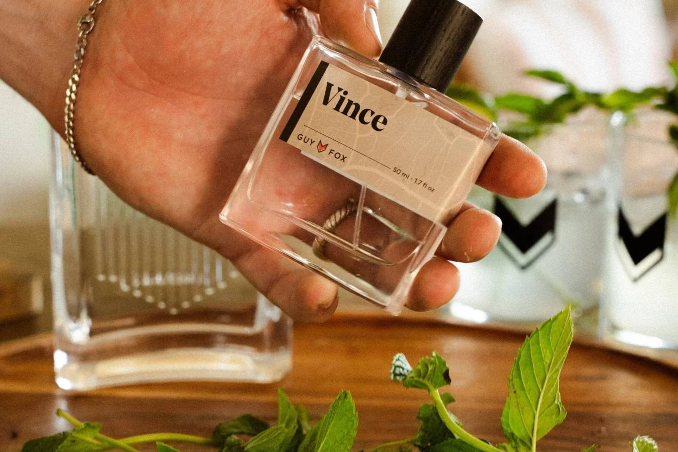 Hand holding the Guy Fox Vince Cologne bottle over a tray of mint and drinks