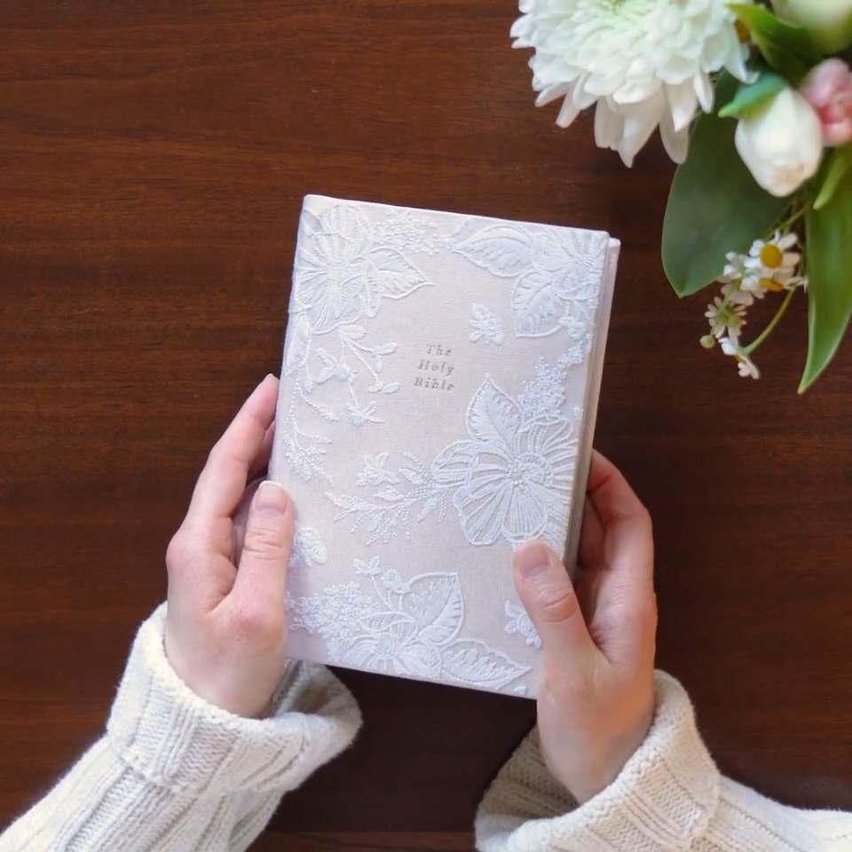 Hands holding the Hosanna Revival NLT Compact Bible Casablanca theme over a wooden table with flowers