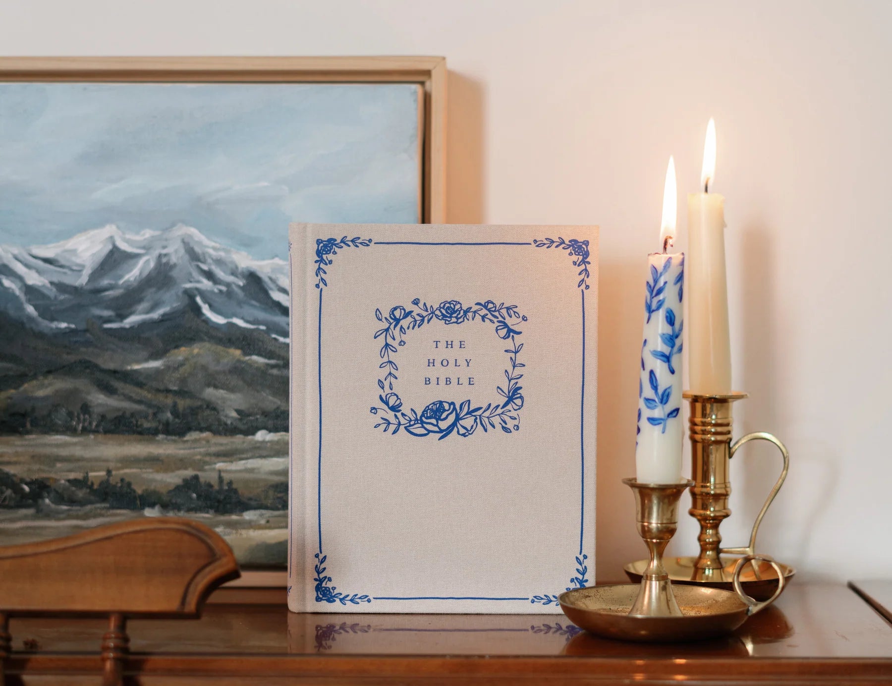 Hosanna Revival NLT Notetaking Bible Adelaide theme on a wooden dresser with candlesticks and a landscape painting