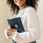 Smiling woman in overalls hugging the Hosanna Revival One Thing I Ask prayer journal in Versailles