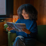 Woman in a blue sweater reading Hosanna Revival Wonder by Alicia Hamilton in a green armchair