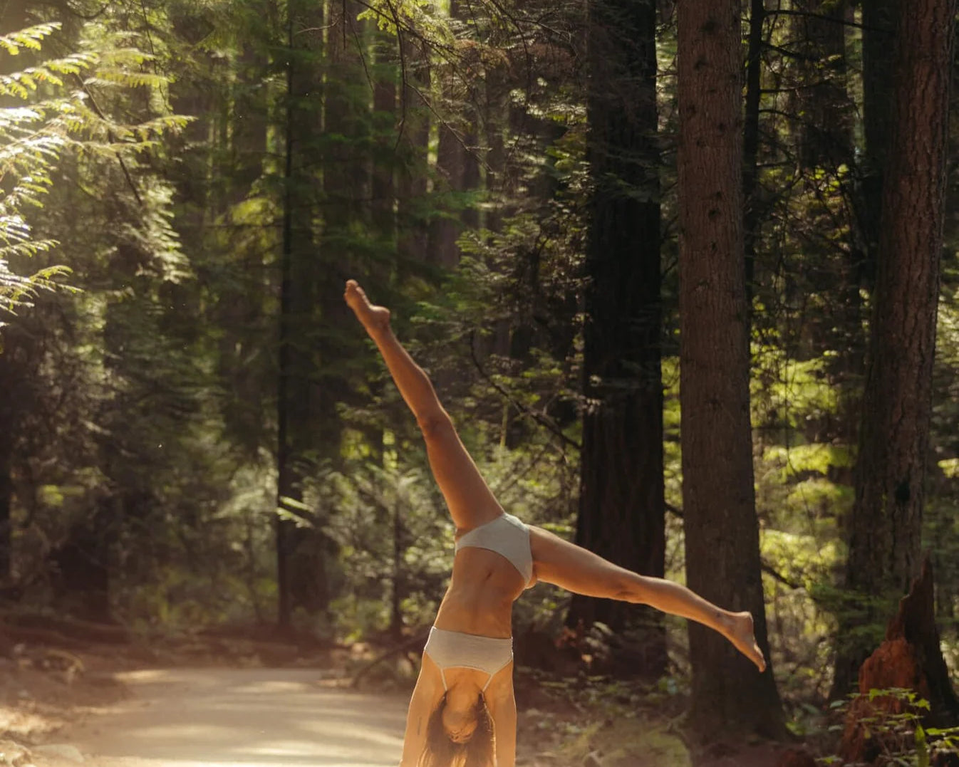 Woman doing a cartwheel on a sunlit forest path wearing the Huha Mineral Bikini underwear in Grey
