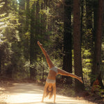 Woman doing a cartwheel on a sunlit forest path wearing the Huha Mineral Bikini underwear in Grey