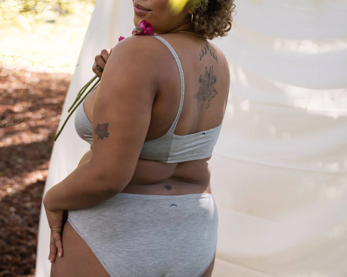 Woman glancing over her shoulder outdoors wearing the Huha Mineral Bikini underwear and bralette in Grey