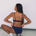 Woman crouching with her back to the camera wearing the Huha Mineral Bikini underwear in Navy