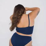 Back view of a woman with wavy hair wearing the Huha Mineral Bikini underwear and bralette in Navy