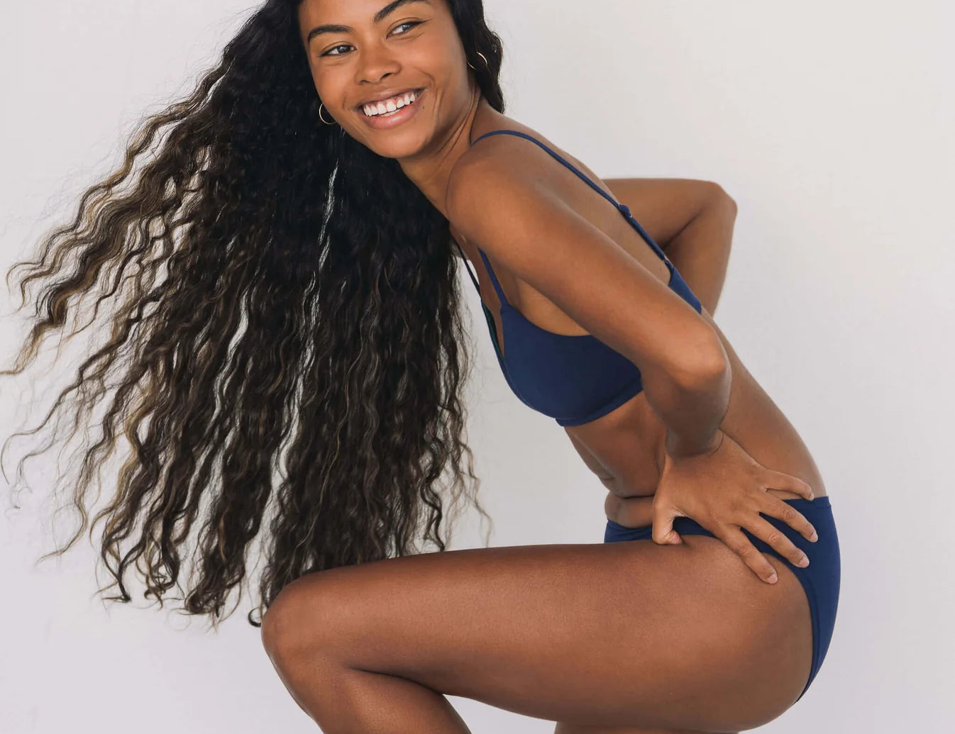 Smiling woman with long curly hair wearing the Huha Mineral Bikini underwear and bralette in Navy