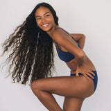Smiling woman with long curly hair wearing the Huha Mineral Bikini underwear and bralette in Navy